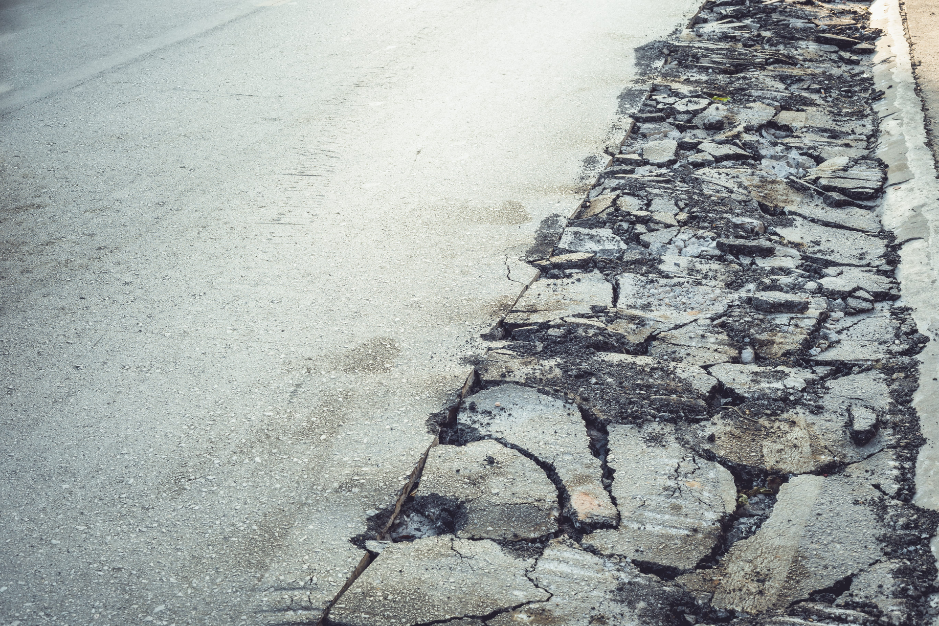Cracked asphalt road edge beside a smooth gray pavement surface
