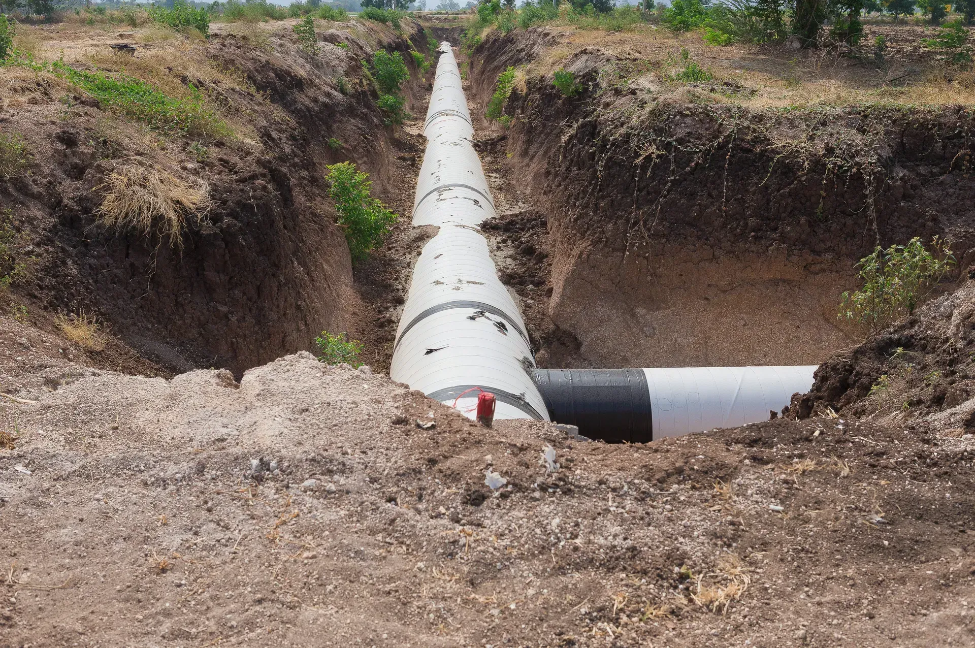 Large white pipeline laid in a dug trench, crossing a dirt excavation site.