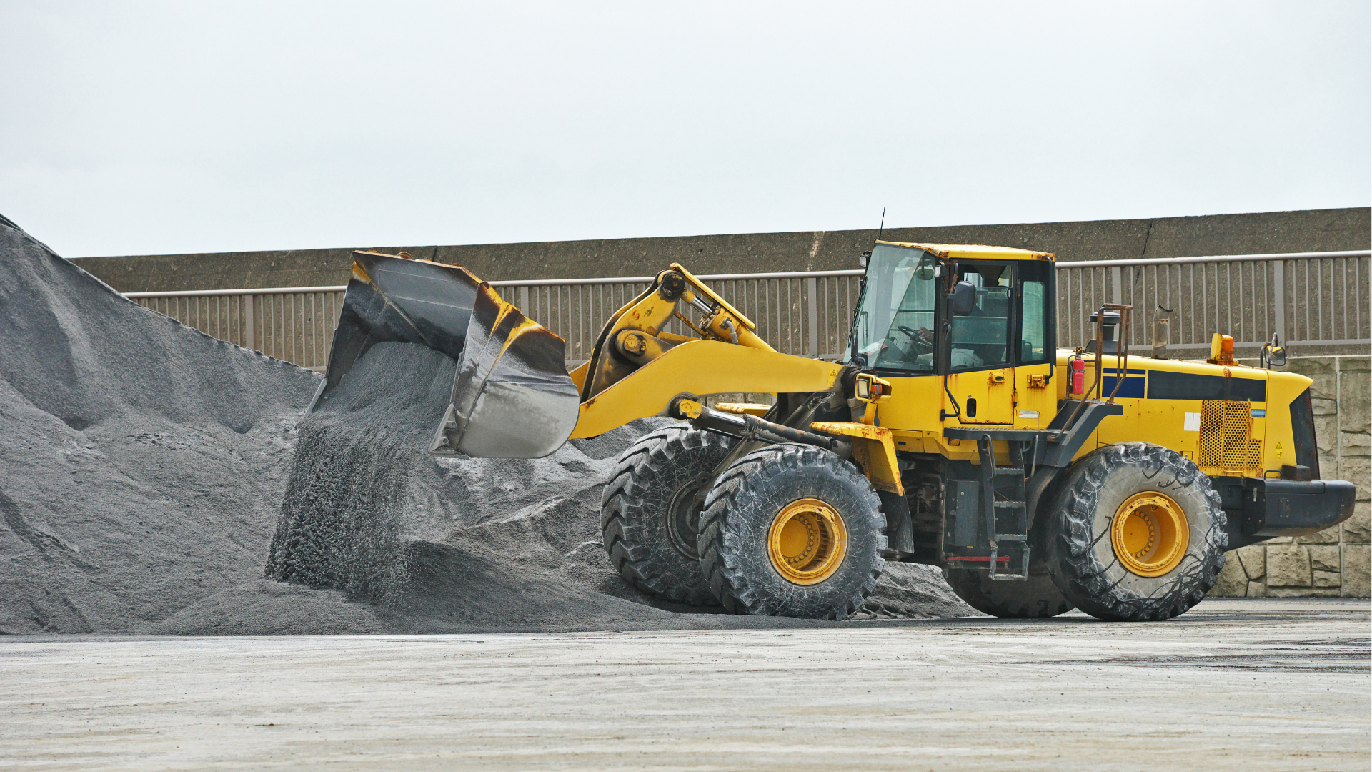 Yellow wheel loader dumping gray gravel at an industrial site