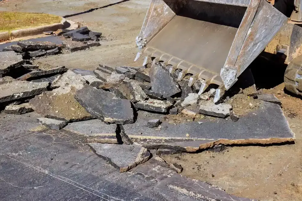 Excavator bucket breaking up dark pavement on a construction site