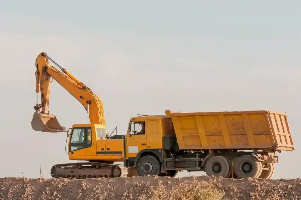 Yellow excavator loading dirt into an orange dump truck at a construction site