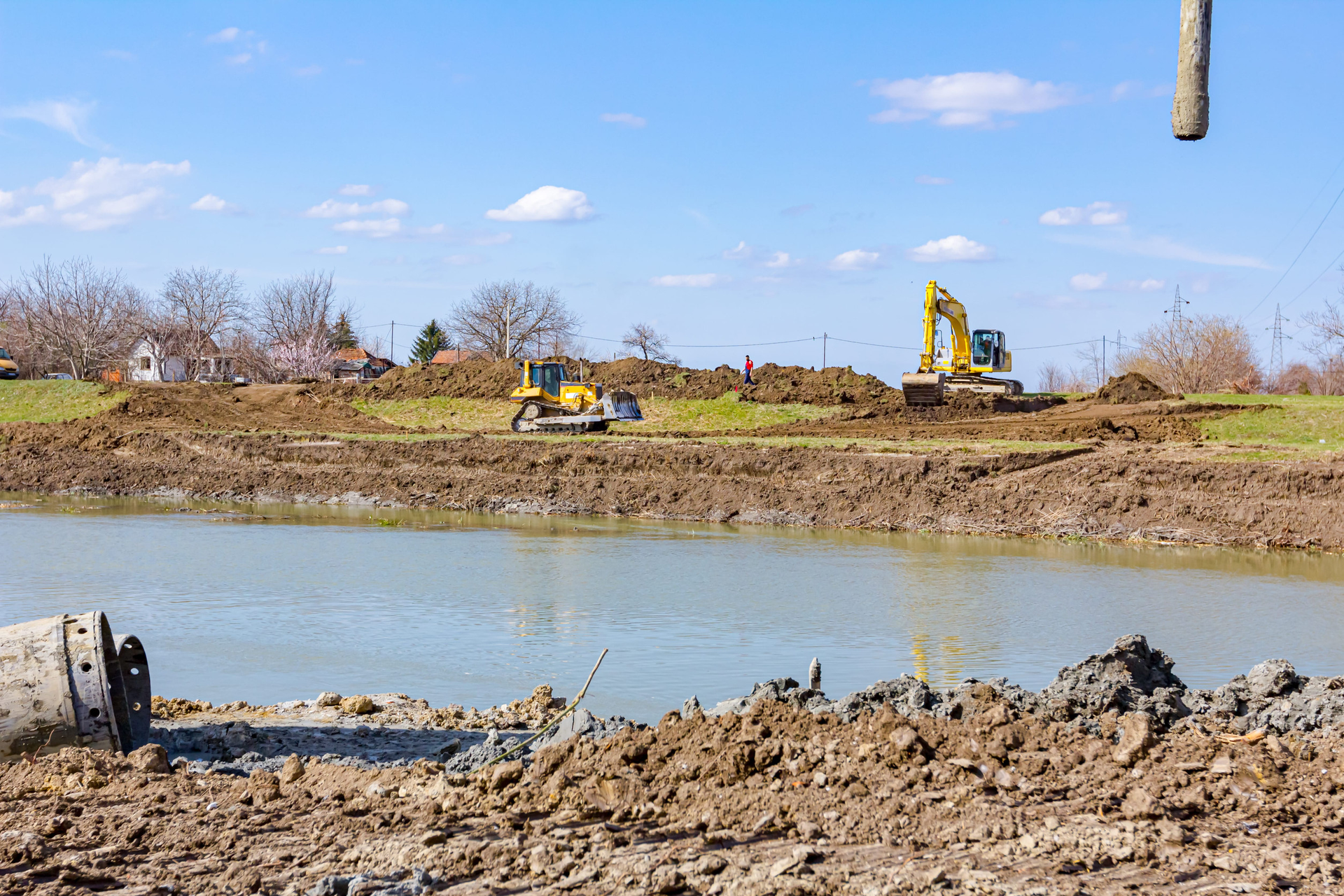 Construction excavators working beside a muddy river under a clear blue sky