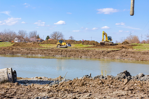Construction excavators working beside a muddy river under a clear blue sky