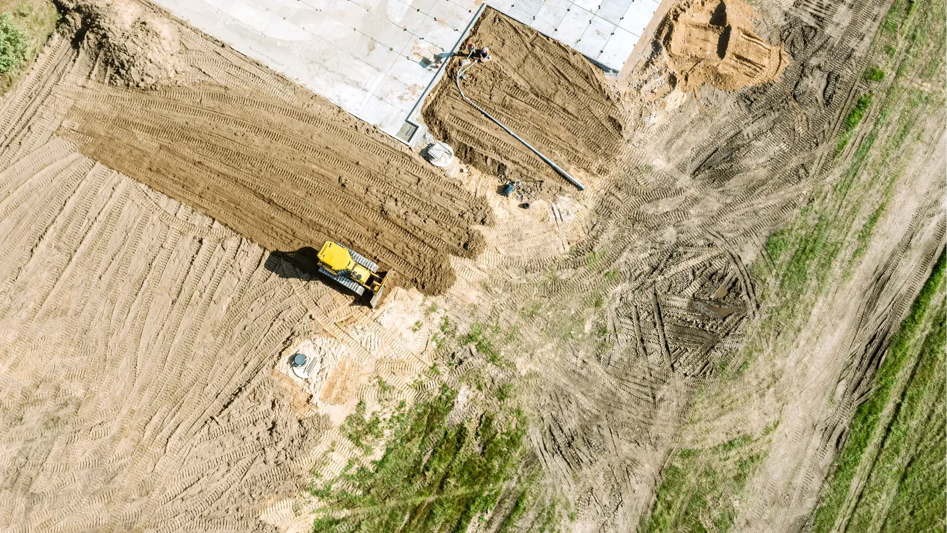 Aerial view of a yellow tractor moving soil on a dirt construction site beside a white structure.