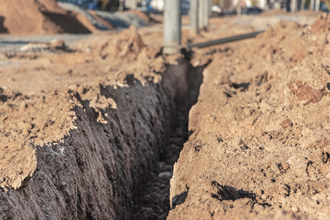 A deep trench cut through dry, sandy soil at a construction site
