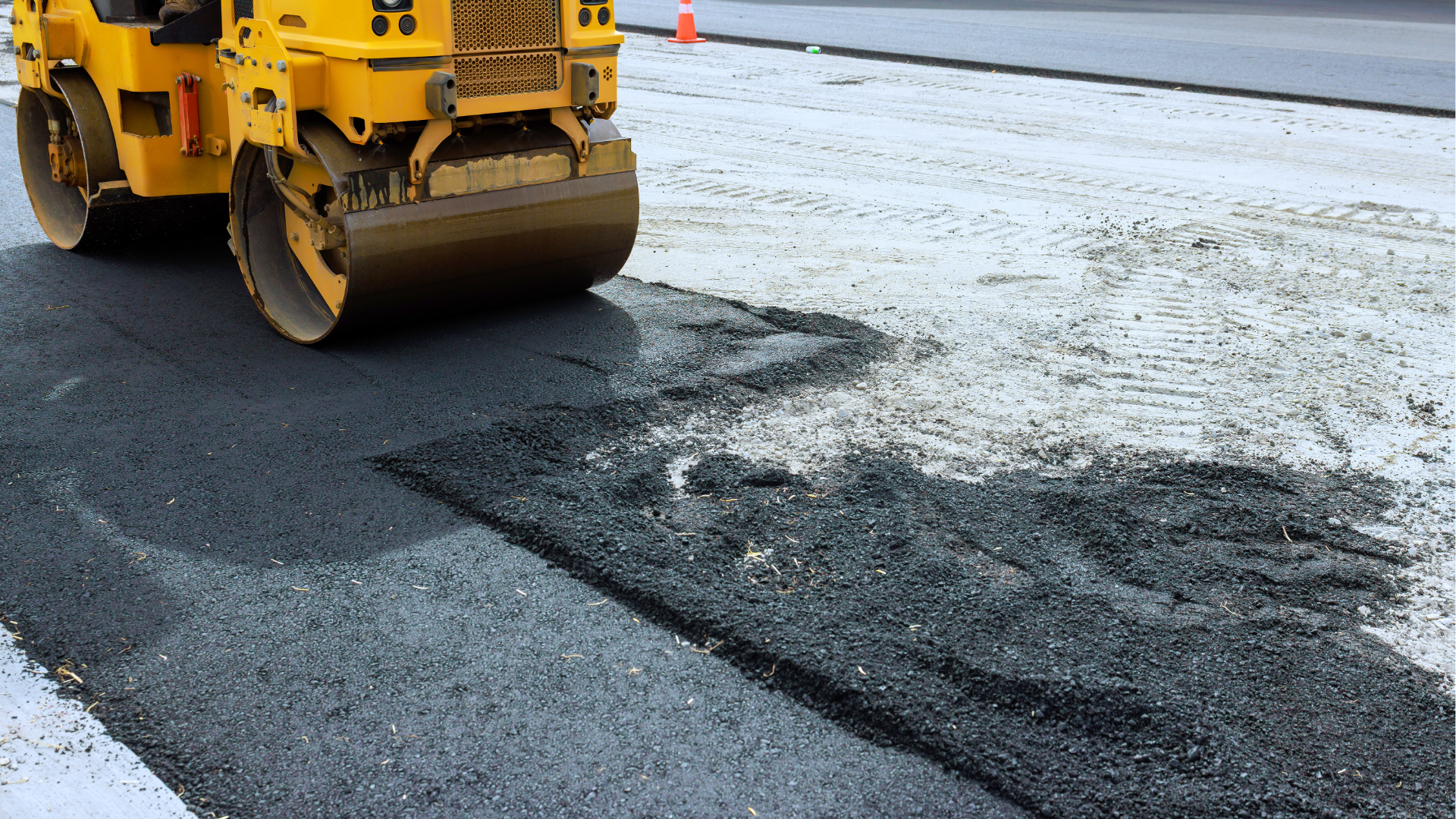 Yellow road roller paving dark asphalt on a street with snow at the edge