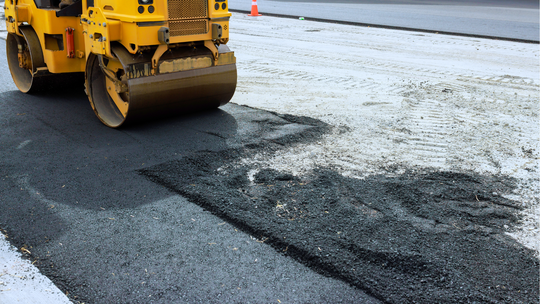 Yellow road roller paving dark asphalt beside a lighter roadway surface