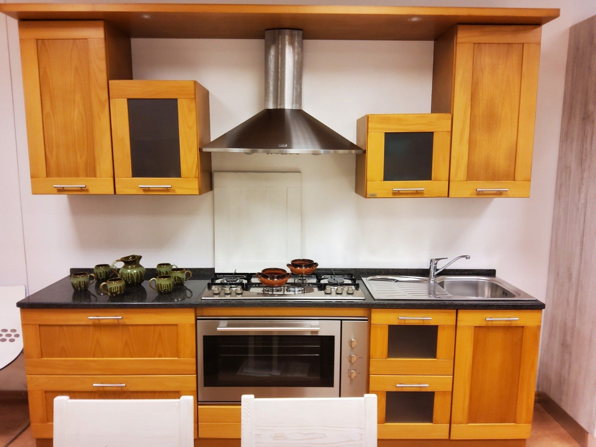 Cucina con mobili in legno chiaro, elettrodomestici in acciaio inossidabile e piano di lavoro nero.