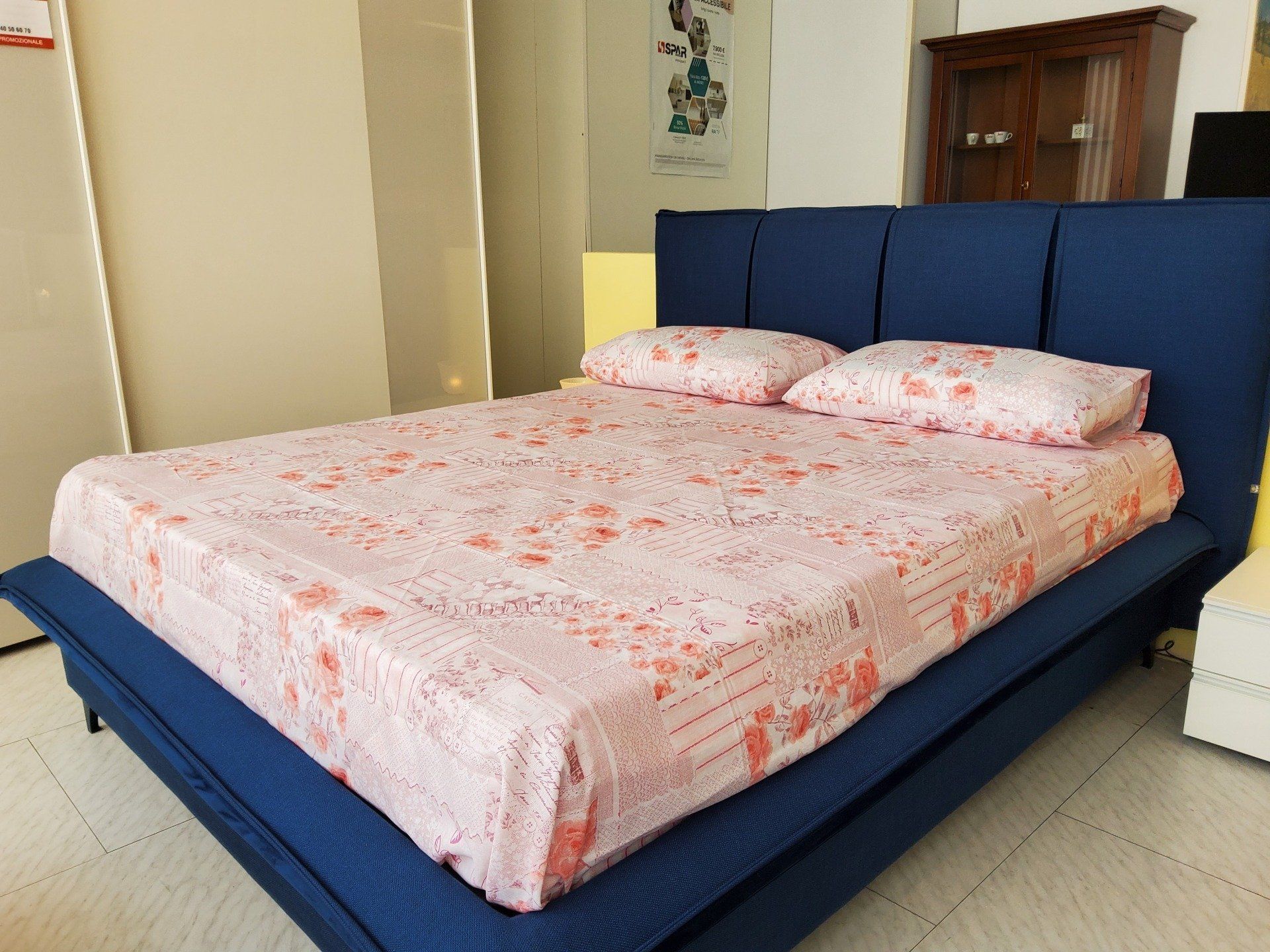 Letto imbottito blu con lenzuola e cuscini rosa a fantasia in uno showroom di mobili.