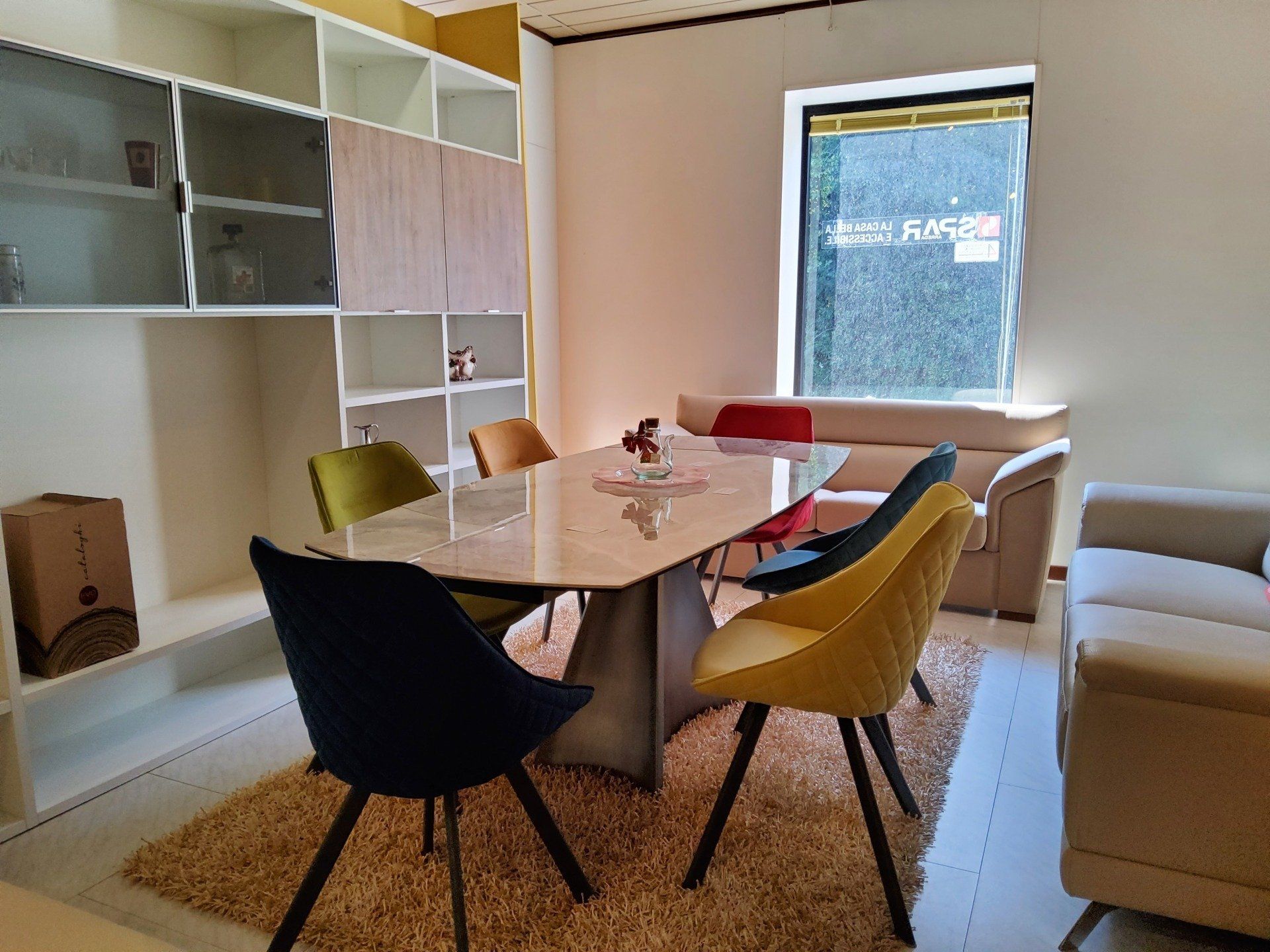 Sala da pranzo con tavolo in marmo, sedie colorate e scaffalature integrate.