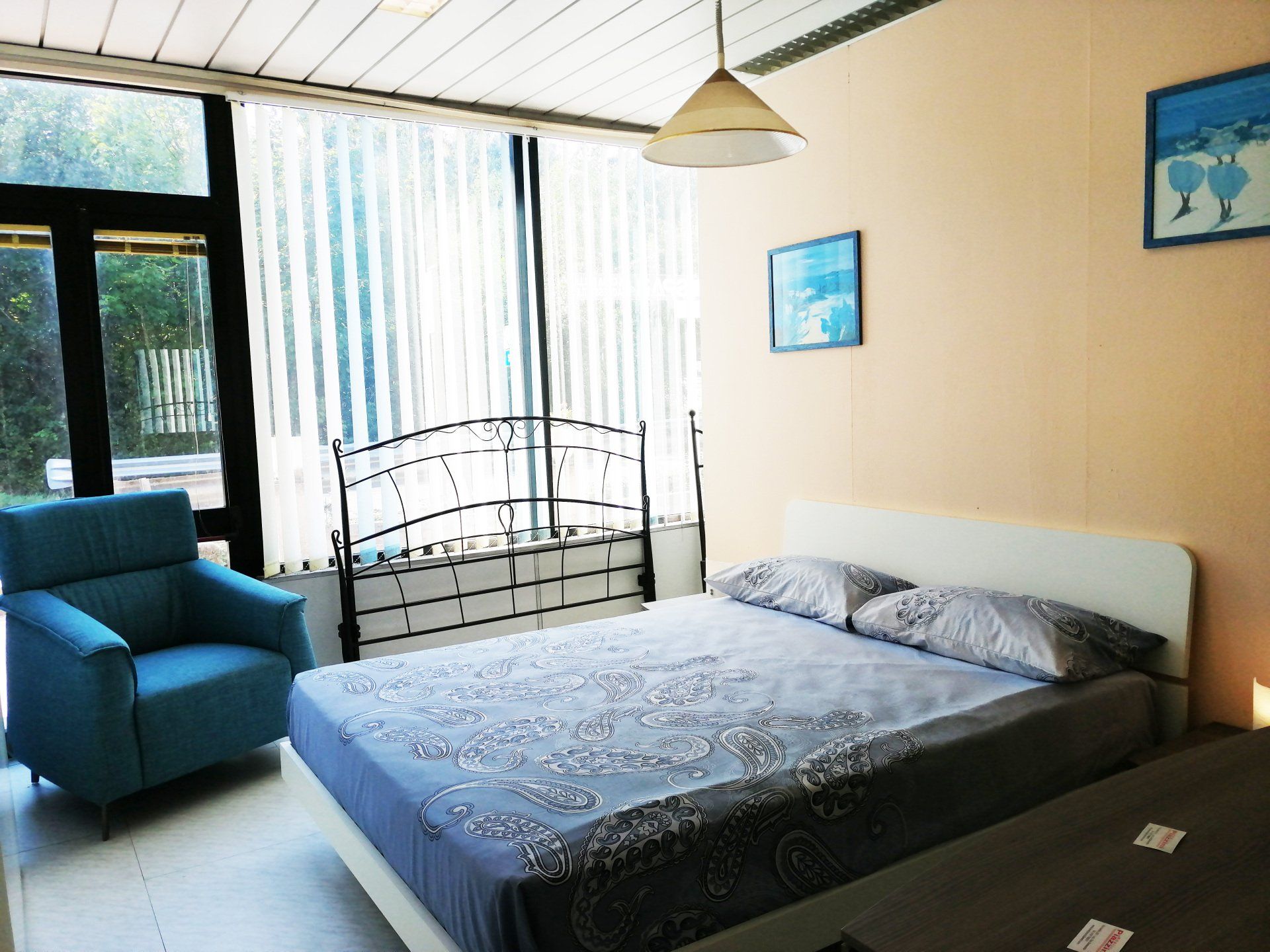 Camera da letto con letto, poltrona blu e ampie finestre con persiane.