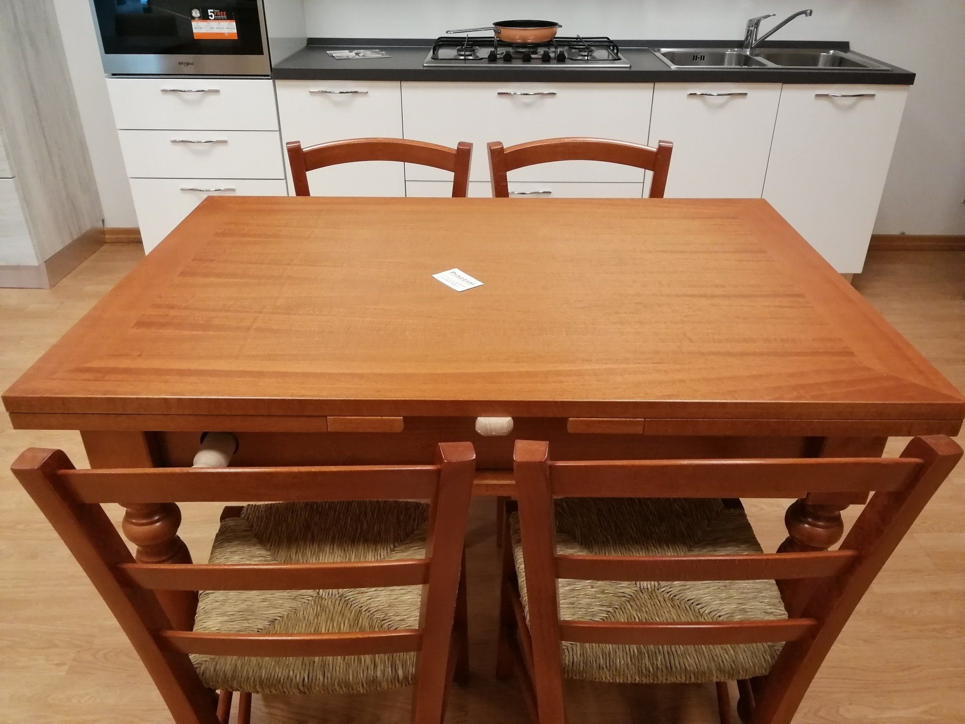 Tavolo da pranzo in legno con quattro sedie di fronte a una cucina con mobili bianchi.