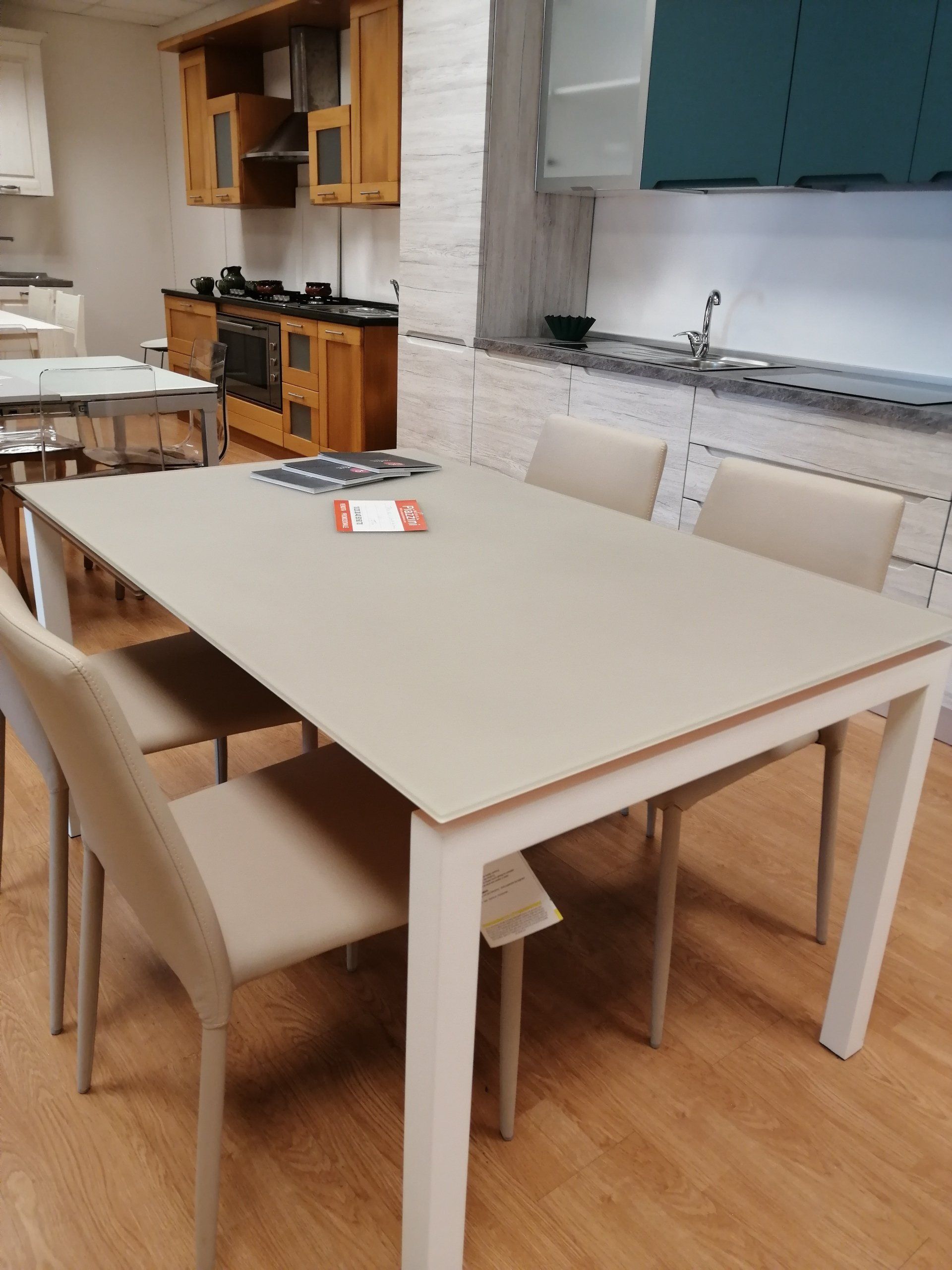 Tavolo da pranzo con quattro sedie in uno showroom, pavimento in legno, colori bianco e beige.