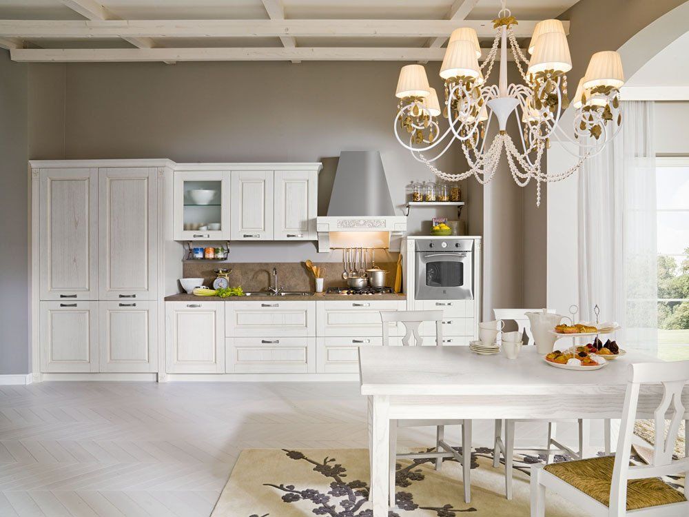 Cucina bianca con tavolo, sedie, mobili, fornelli e lampadario.