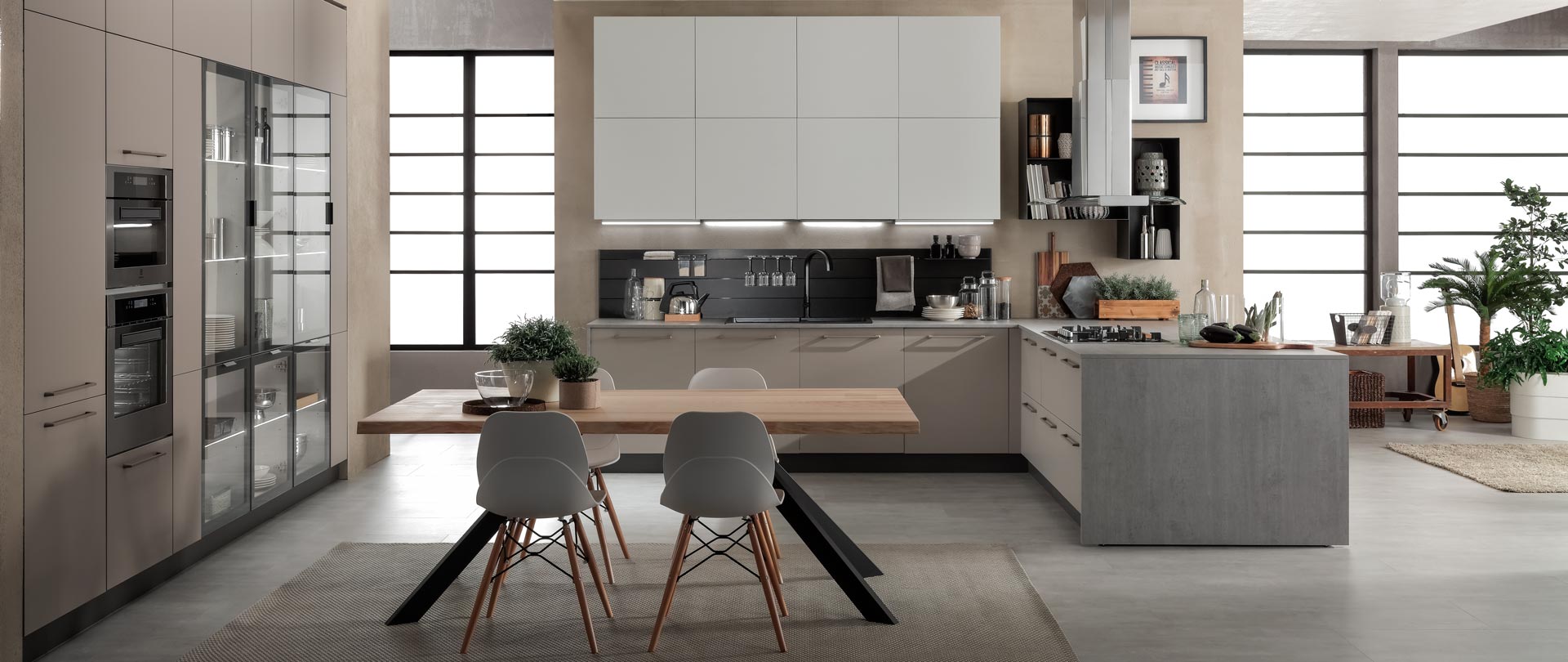 Cucina moderna con mobili in legno chiaro, isola grigia e ampie finestre. Tavolo da pranzo con sedie al centro.