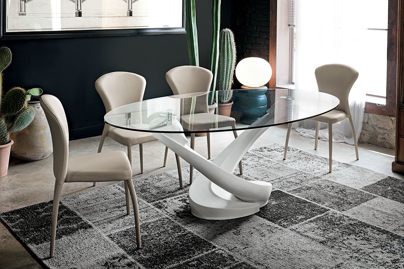 Tavolo da pranzo ovale in vetro con base bianca e sedie beige su tappeto fantasia.