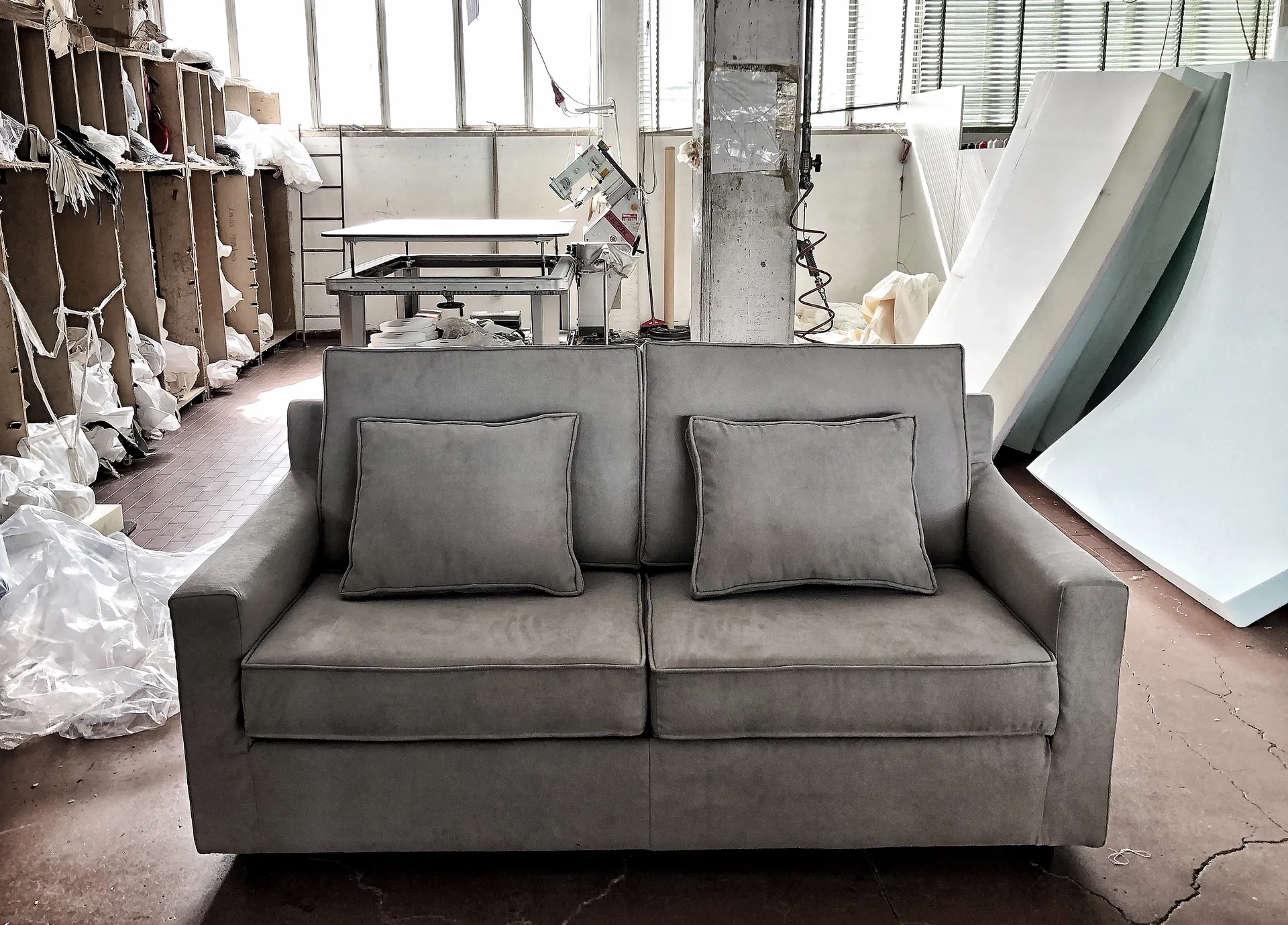 Divano a due posti con due cuscini quadrati in un ambiente industriale. Rivestimento beige.