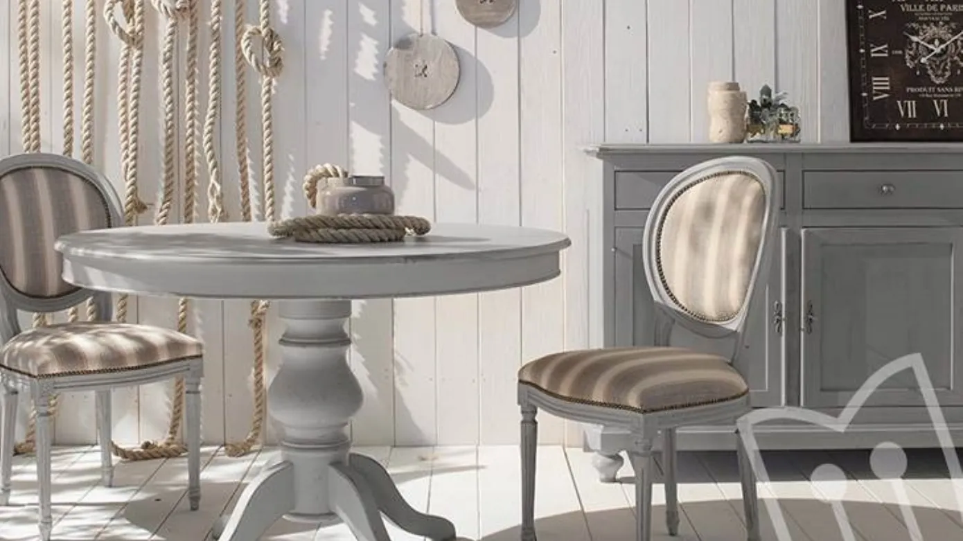 Una sala da pranzo in stile nautico con un tavolo rotondo, due sedie e una credenza, il tutto nei toni del grigio e del bianco.