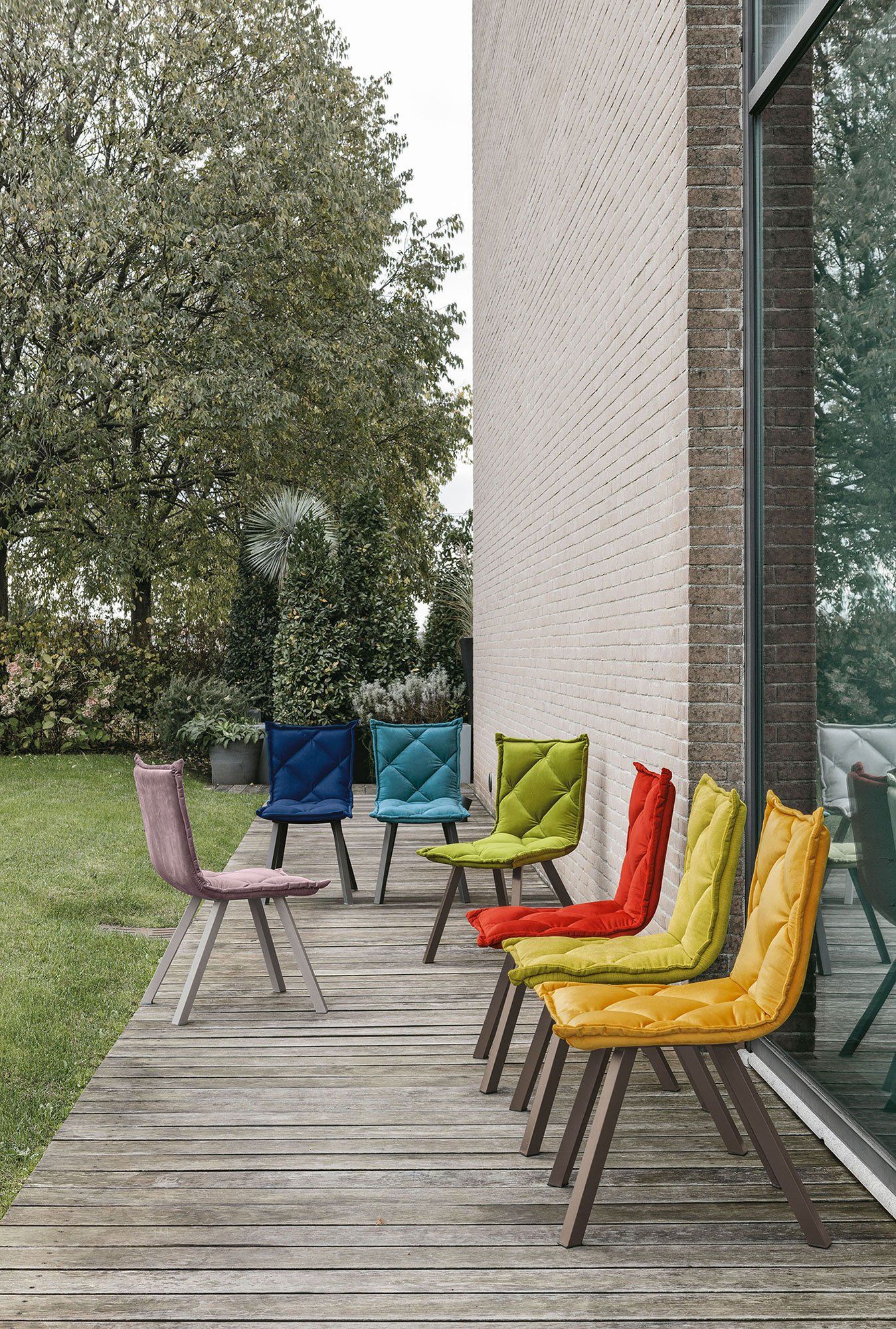Sedie trapuntate colorate su una terrazza in legno vicino a un edificio e a un giardino.