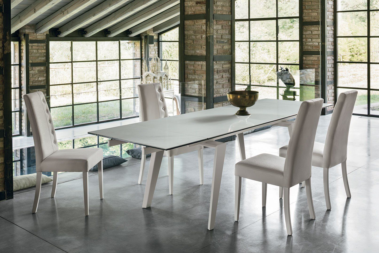 Sala da pranzo: tavolo bianco, quattro sedie imbottite, grandi finestre, colonna in mattoni.