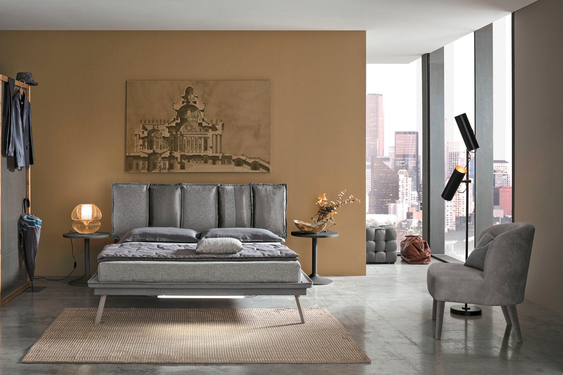 Camera da letto con letto grigio, pareti color cuoio, vista sulla città, poltrona, lampada da terra.