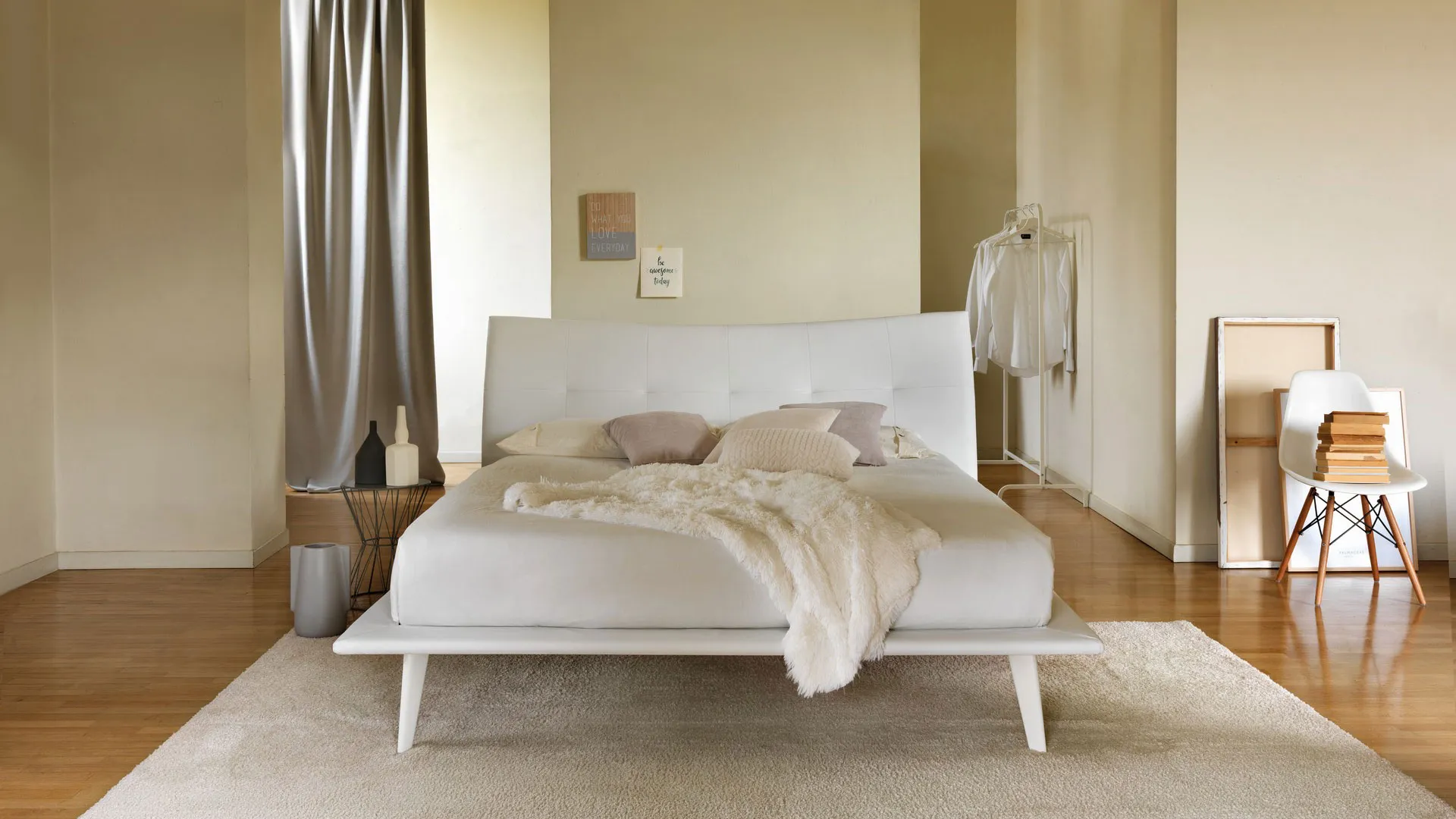 Letto bianco in una camera da letto minimalista con tappeto, pavimento in legno e pareti neutre.
