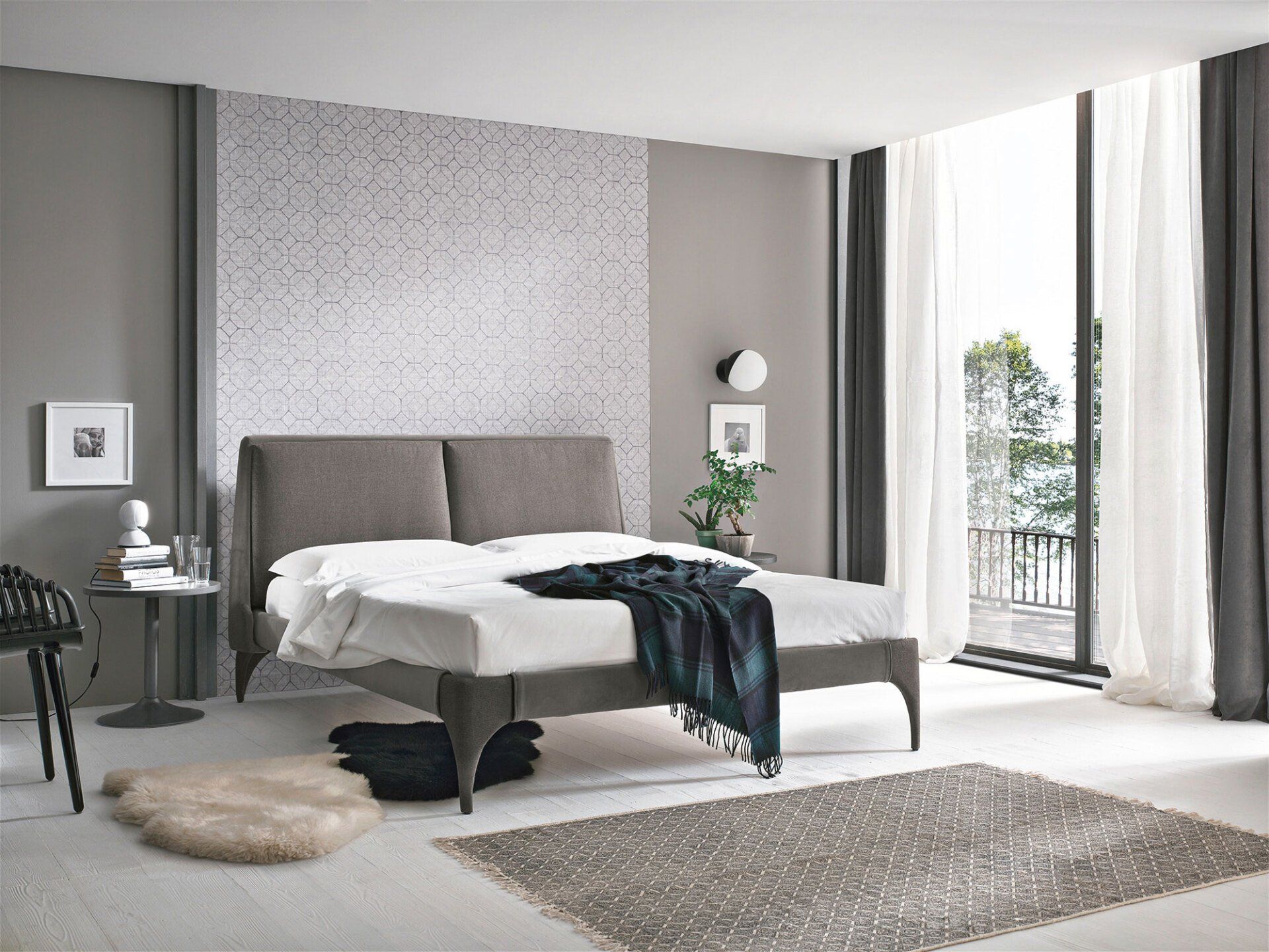 Camera da letto con letto, parete decorata, grande finestra con tende bianche e tappeto.