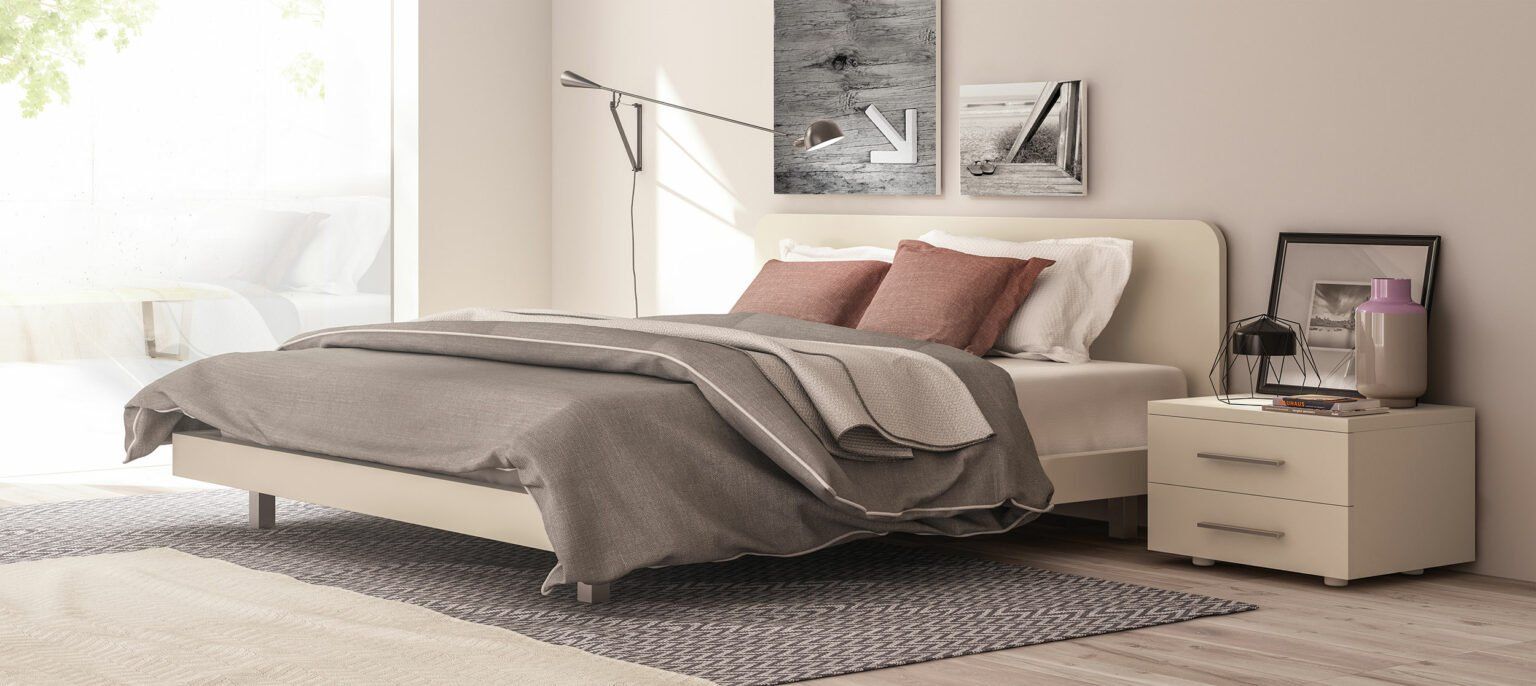 Camera da letto con letto, cuscini, piumone grigio, comodino con lampada e quadri alle pareti.