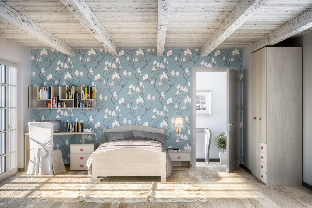 Camera da letto con carta da parati floreale, letto, scrivania, librerie, porta aperta e travi bianche al soffitto.