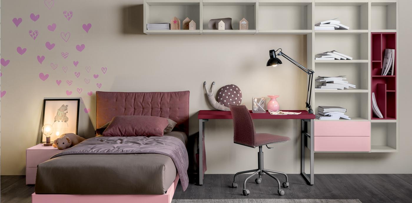 Camera da letto con letto, scrivania, libreria e decorazione murale a forma di cuore. Colori rosa e bordeaux.