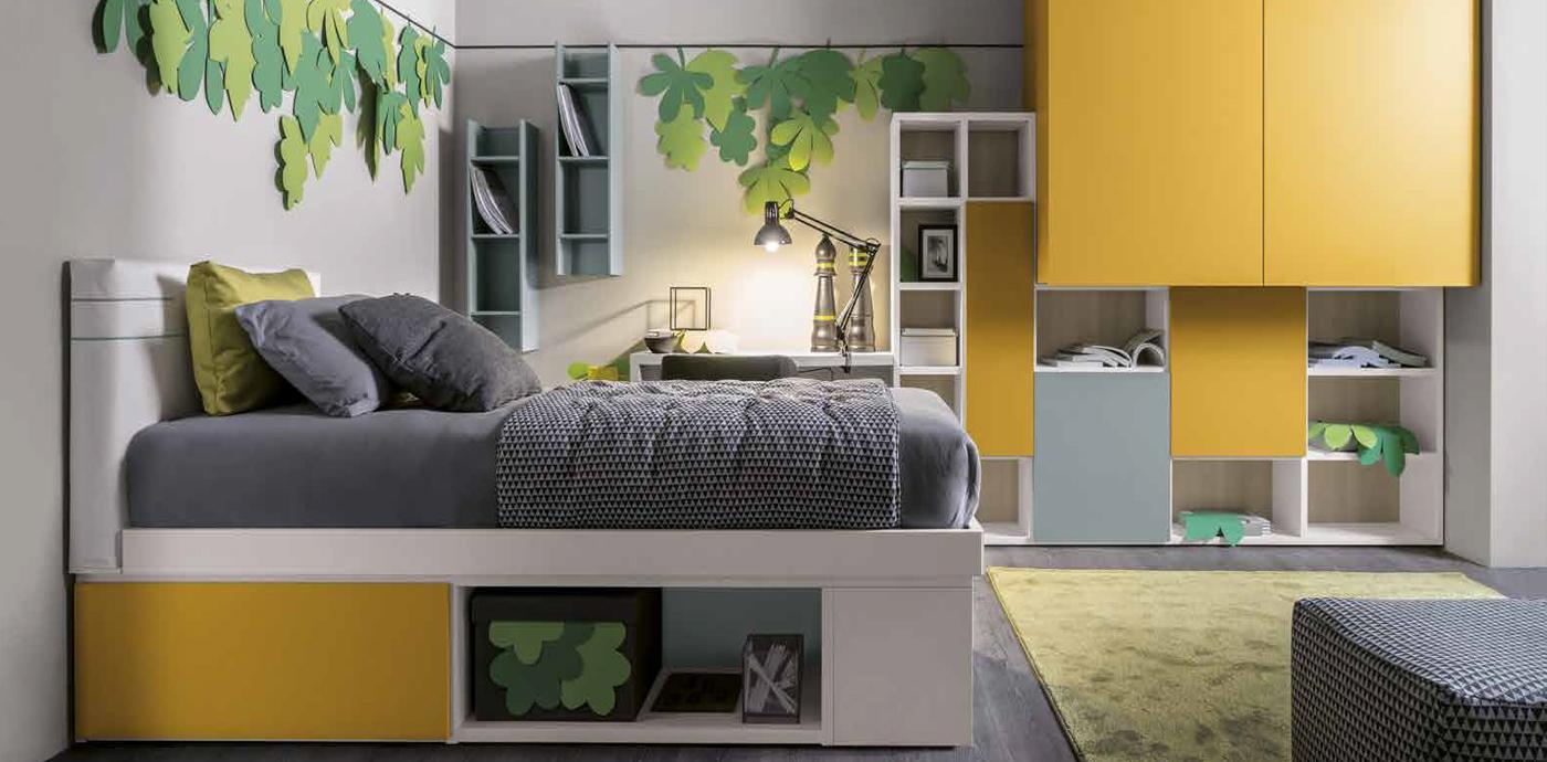 Camera da letto con mobili gialli e bianchi, biancheria da letto grigia e tappeto verde. Foglie decorative alle pareti.