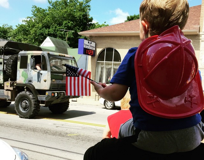 A little boy wearing a fireman 's hat watches a parade