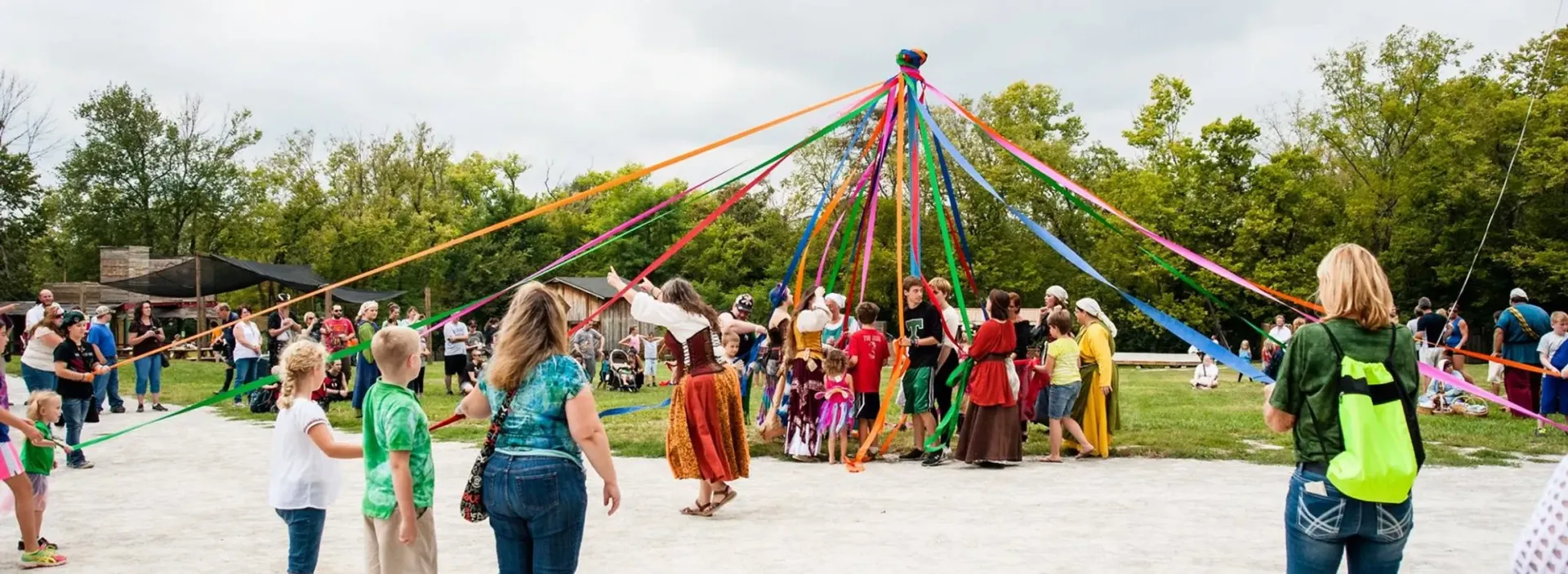 A group of people are dancing around a maypole in a park.