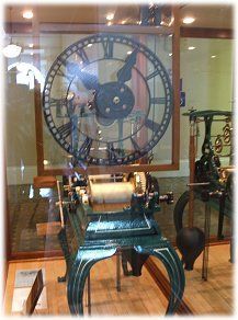 A large clock with roman numerals is on display in a glass case.