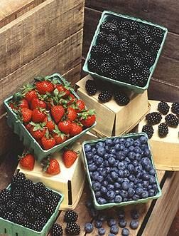 Strawberries , blackberries , blueberries , and raspberries are stacked on top of each other on a wooden table.