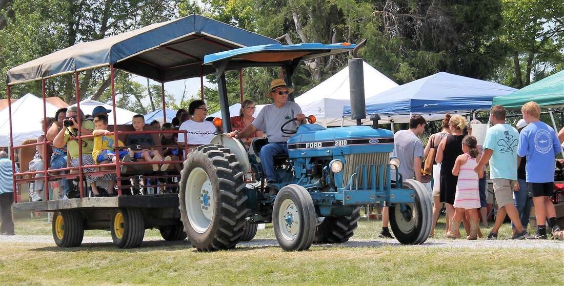 A man is driving a blue tractor with a trailer attached to it.