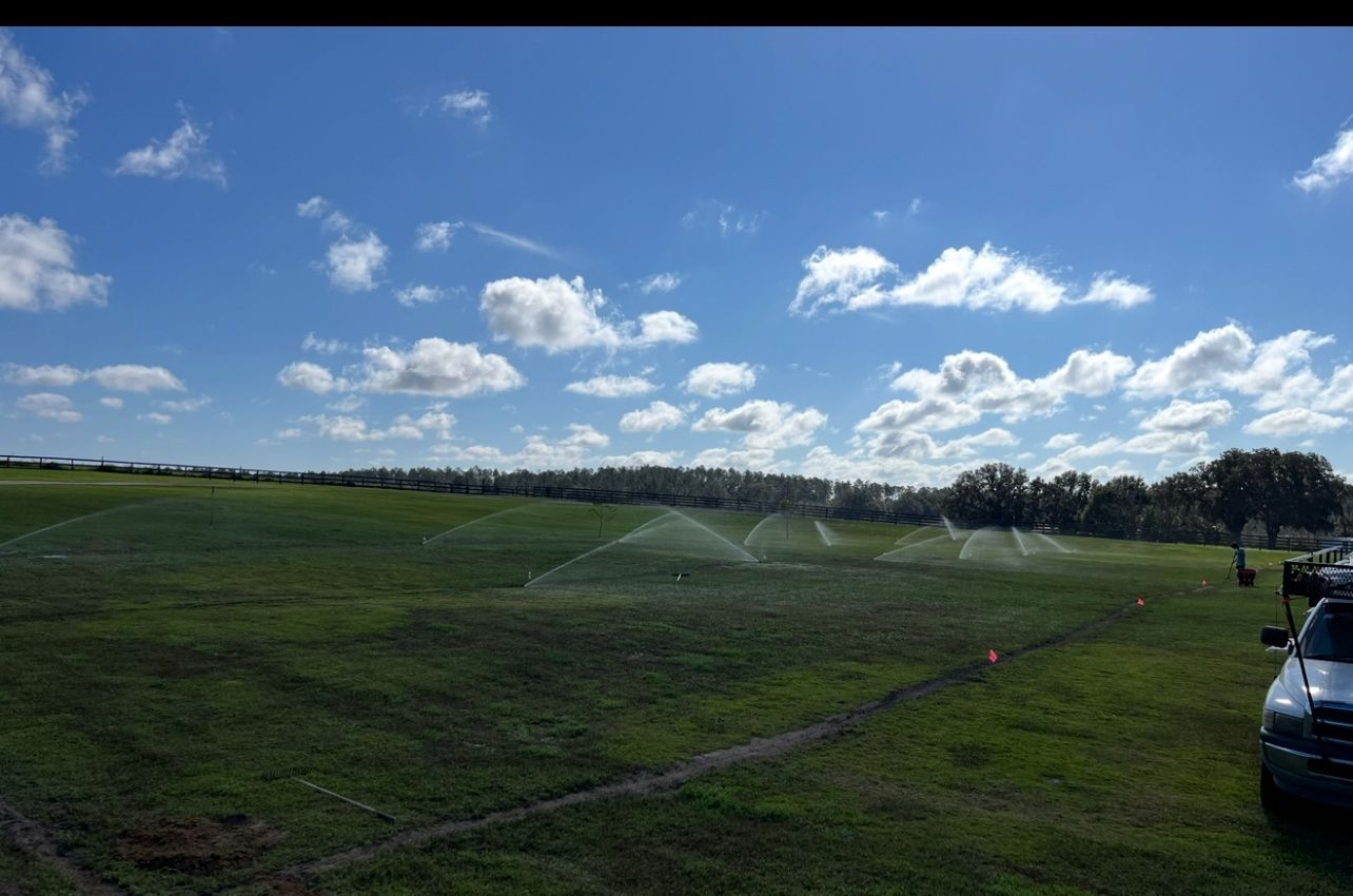 A car is parked in a field with sprinklers spraying water.