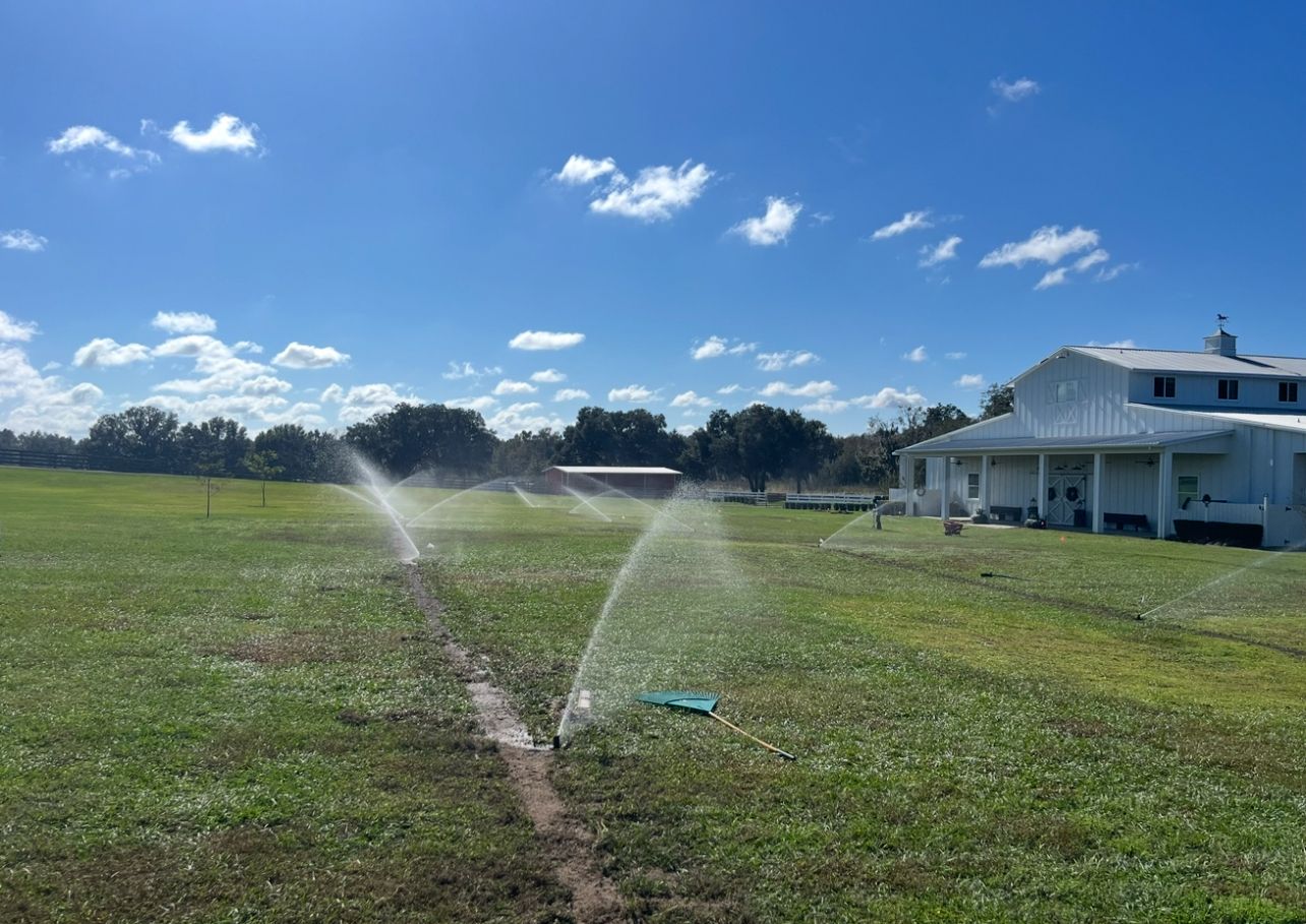 A sprinkler is spraying water on a grassy field in front of a house.