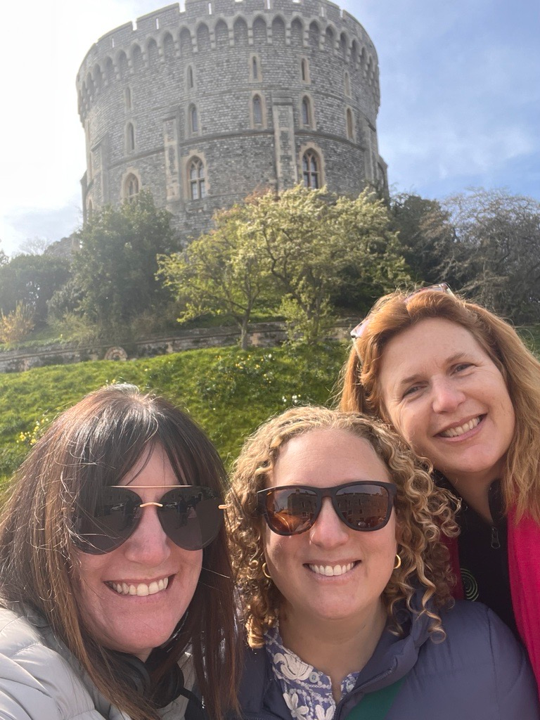 Three women are posing for a picture in front of a castle.