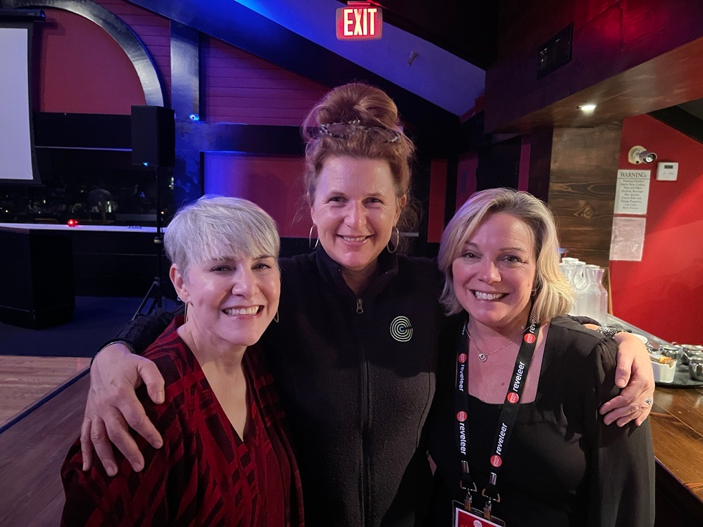 Three women are posing for a picture in front of an exit sign.