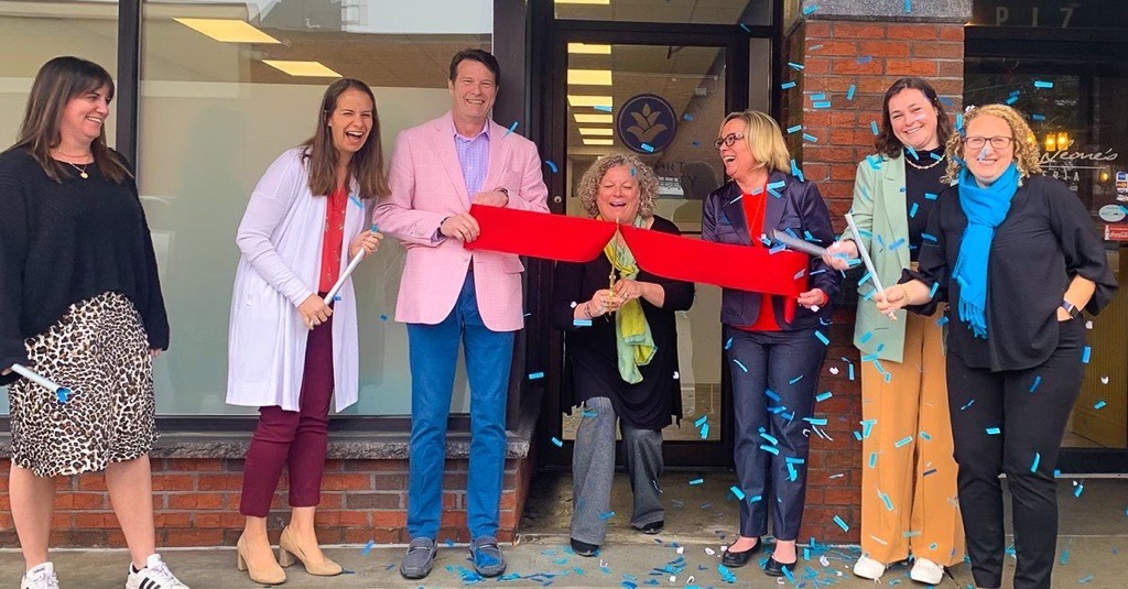A group of people are cutting a red ribbon in front of a building.
