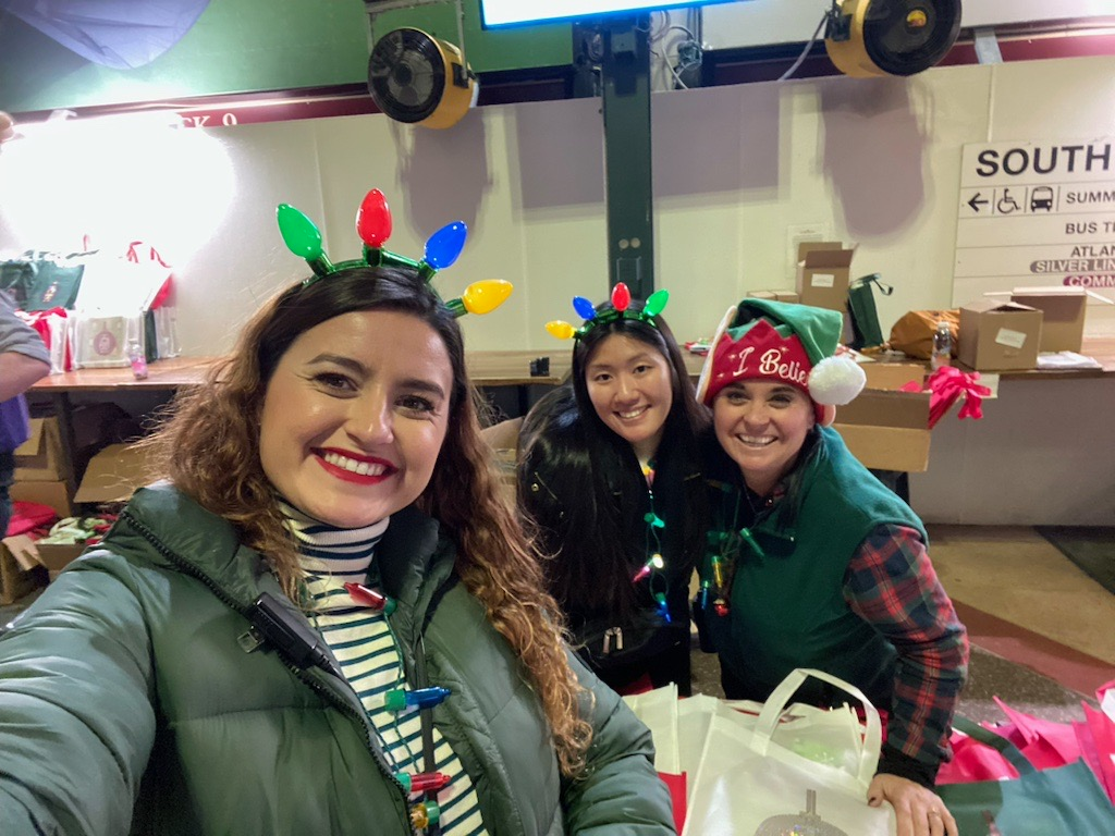 Three women are posing for a selfie in a room with christmas lights on their heads.