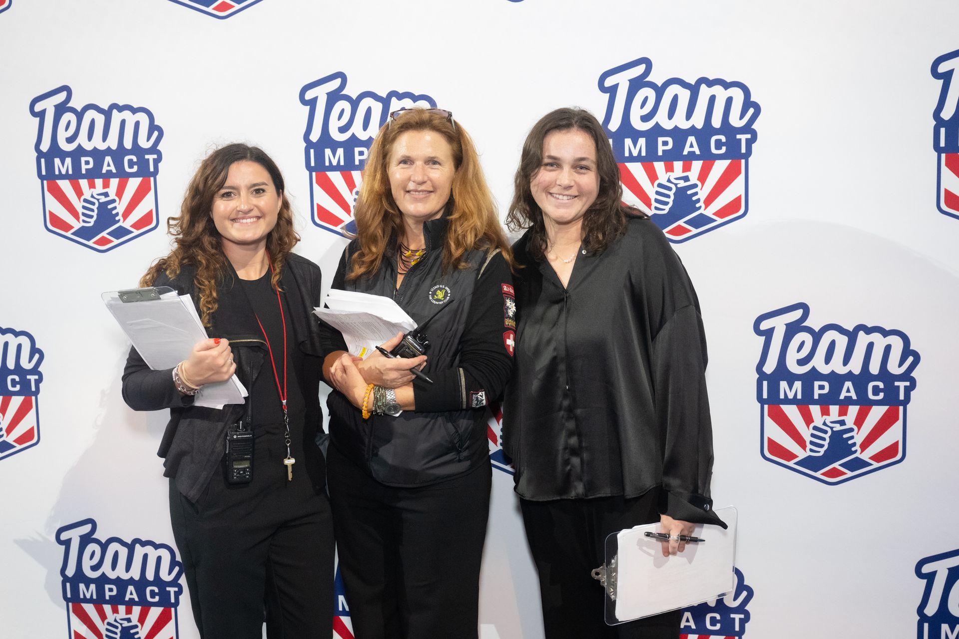 Four women are posing for a picture in front of a team impact wall.