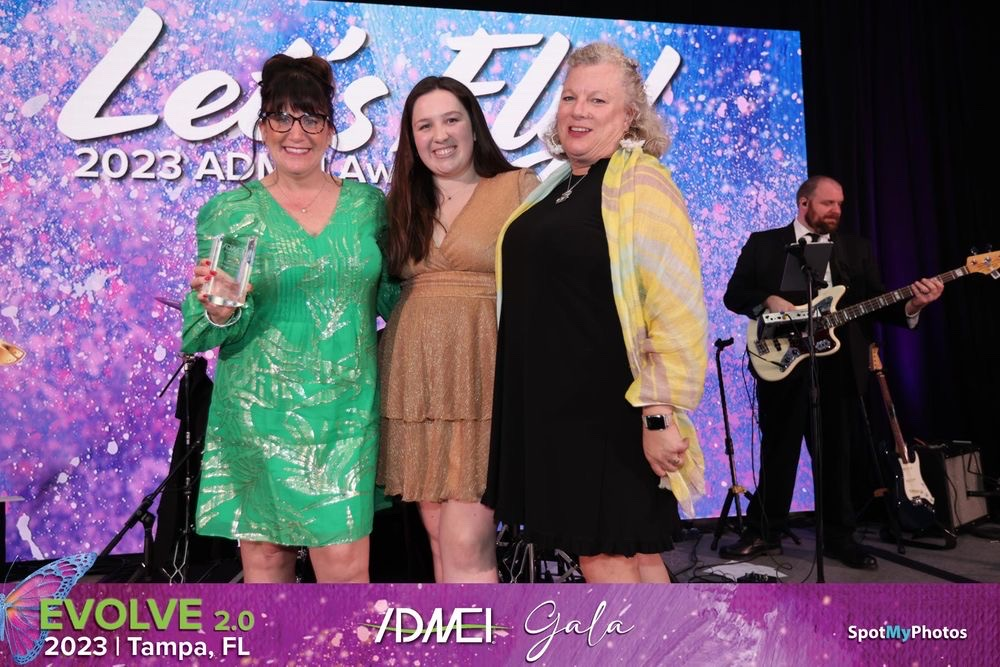 Three women are posing for a picture in front of a large screen.
