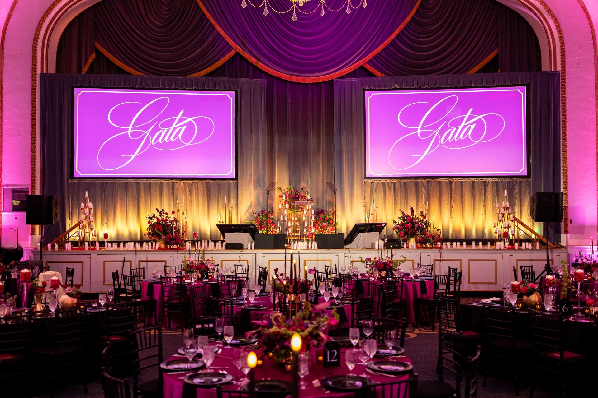 Elegant banquet hall with purple-lit stage, floral decor, and “Lyda” displayed on twin screens