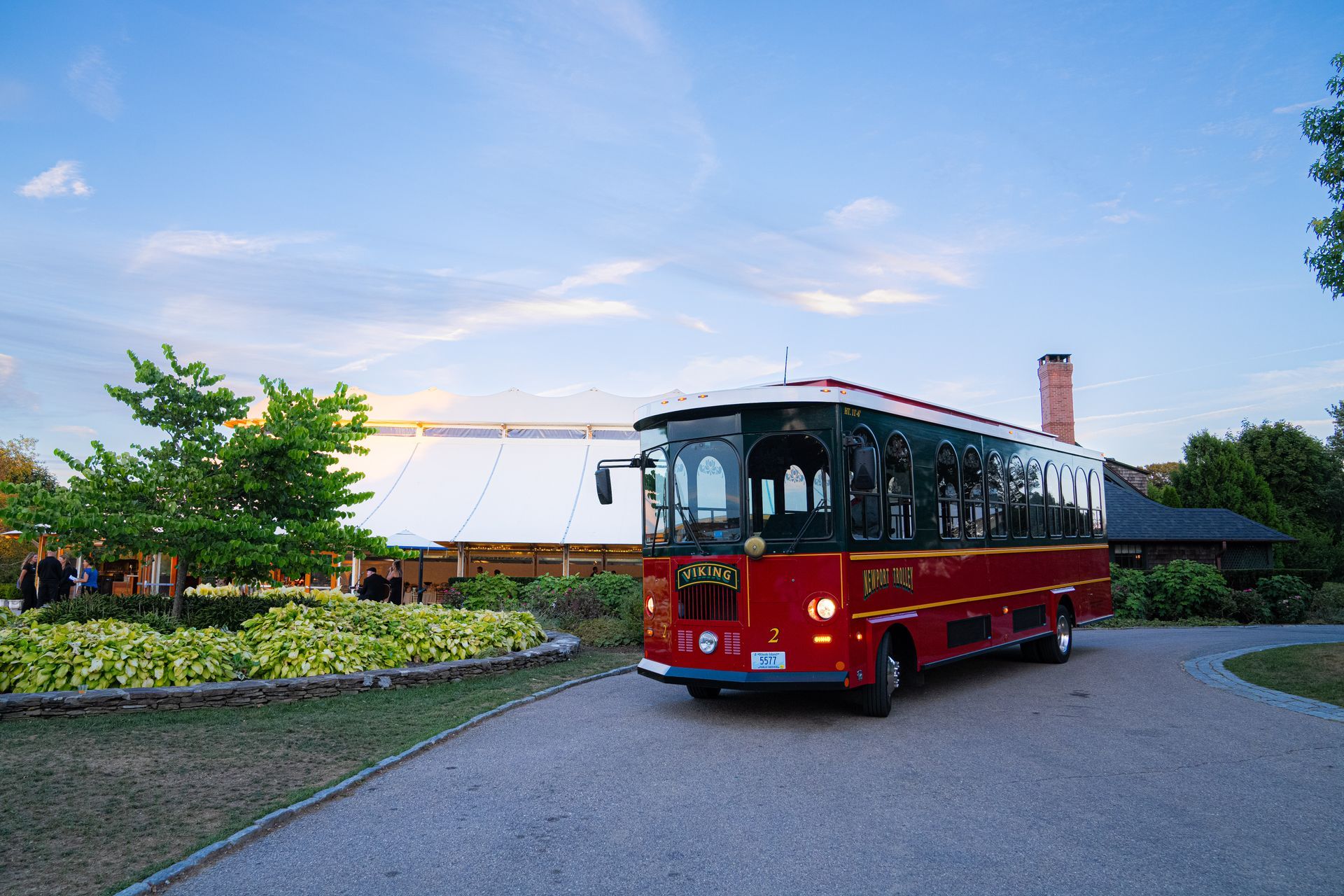 Red trolley on gravel driveway; white tent and brick building in background.