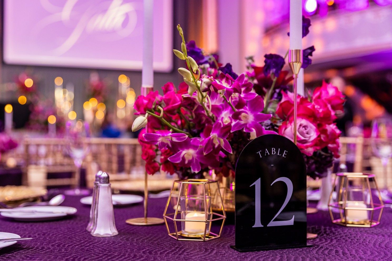 A table set for a wedding reception with purple flowers and candles.