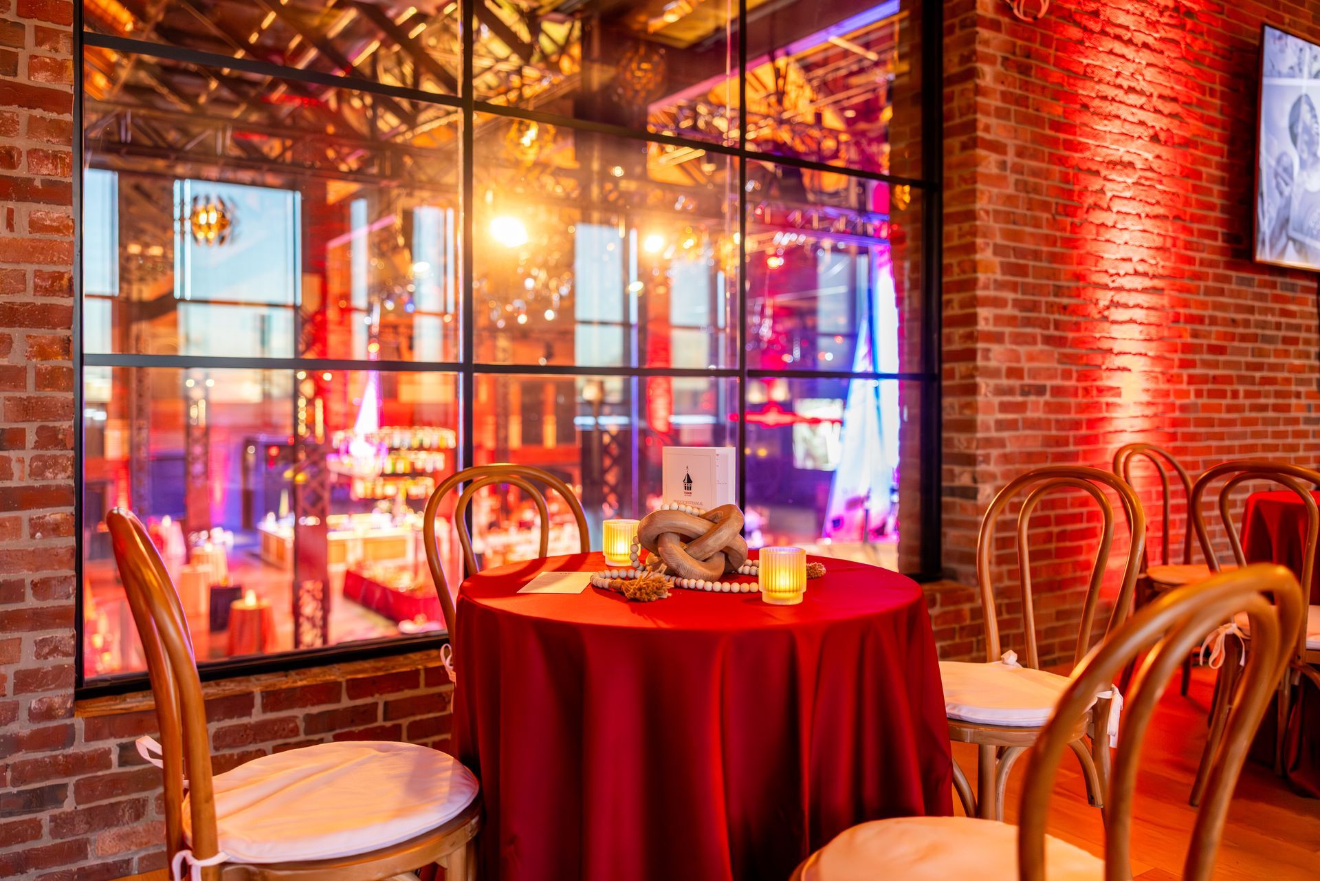 A table set for dining in a room with a large window and brick walls, illuminated in red.
