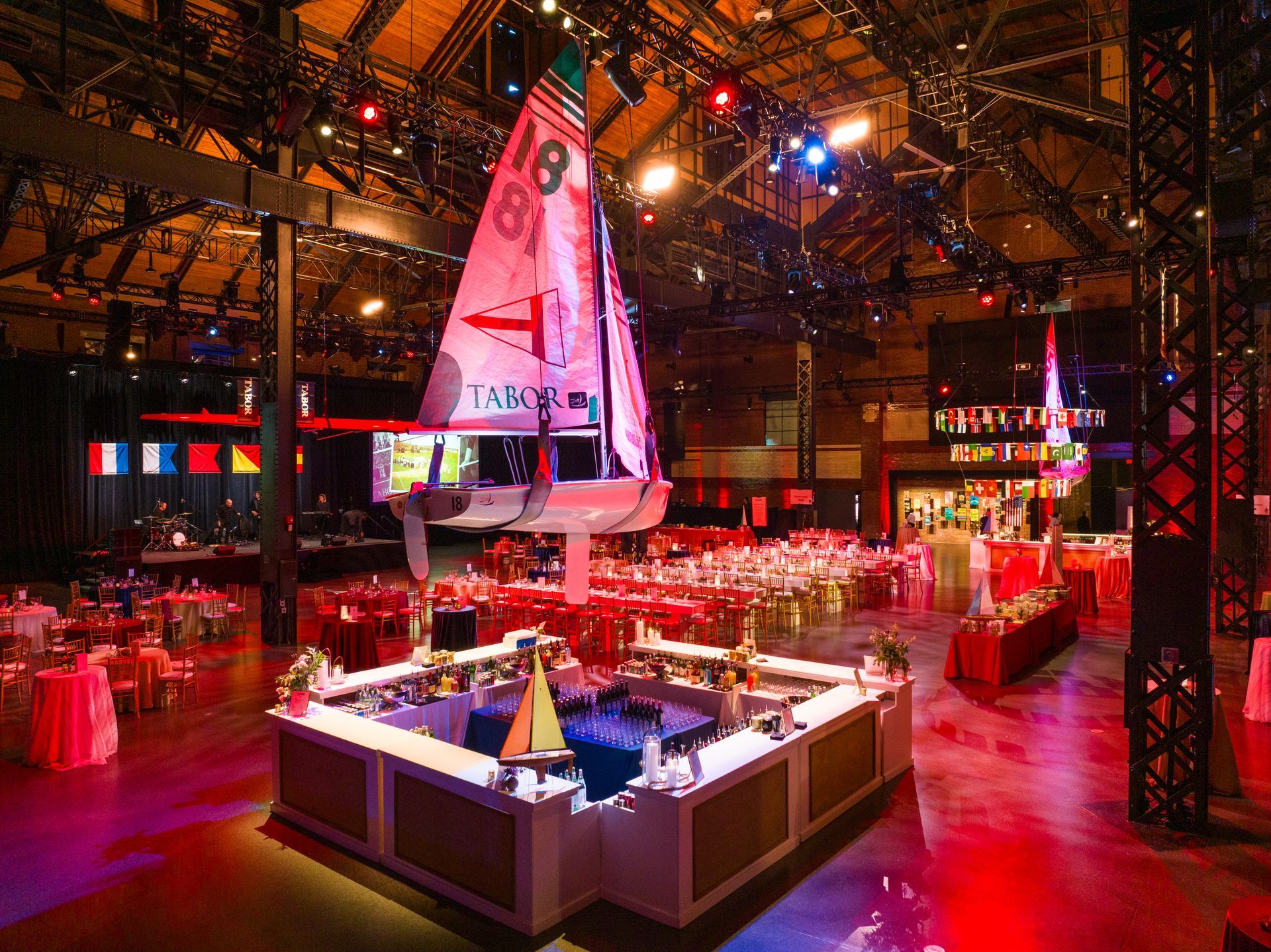 Large event space with sailboat decor, tables, bars, and red and white lighting.