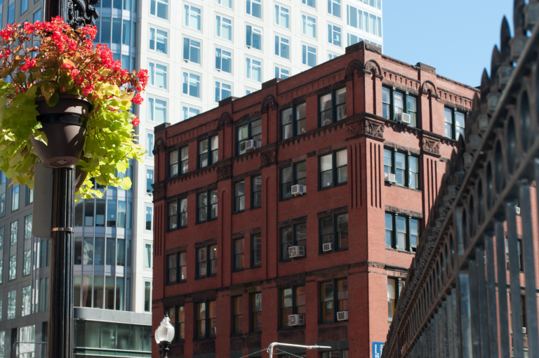 Red brick building in city with hanging flower basket and fence.